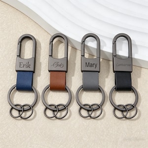 Pode incluir: Quatro porta-chaves personalizados com os nomes Erik, Ted, Mary e Catherine. Cada porta-chaves apresenta um fecho metálico e uma correia de couro em azul, castanho, cinzento e preto. Os porta-chaves têm dois anéis metálicos para chaves.