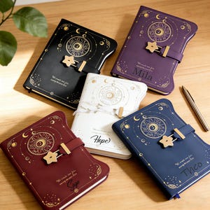 Könnte beinhalten: Eine Sammlung dekorativer Journale in verschiedenen Farben, darunter Schwarz, Burgunderrot, Weiß, Lila und Marineblau. Jedes Journal hat ein himmlisches Design mit goldenen Akzenten, einen sternförmigen Verschluss und die Inschrift "We create our fate every day we live."