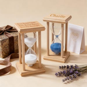 Pode incluir: Duas ampulhetas de madeira com lâmpadas de vidro transparente, uma com areia branca e outra com areia azul. A parte superior de uma ampulheta diz "Every Second Counts Every Moment Matters Every Day Meaningful." A outra diz "Charlie."