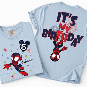 May include: Two light blue t-shirts. One features a cartoon Spider-Man with a balloon that says "5" and the name "Oliver". The other shirt has "IT'S MY BIRTHDAY" and a Spider-Man graphic on the back. Both shirts have a crew neck.