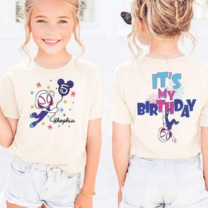 May include: A beige t-shirt featuring a Spider-Gwen graphic holding a Mickey Mouse-shaped balloon with the number 5. The front of the shirt has the name "Shophia" below the graphic. The back of the shirt says "It's My Birthday" with a Spider-Gwen graphic.