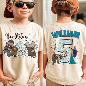 Puede incluir: Una camiseta beige de manga corta con un estampado gr&aacute;fico. El frente muestra el texto Birthday Boy con personajes de dibujos animados. La parte posterior presenta el nombre William sobre un n&uacute;mero 5 grande, rodeado de copos.