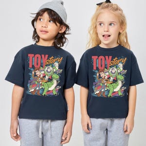 May include: Two children wearing navy blue t-shirts with a "Toy Story" graphic. The graphic features Woody, Buzz Lightyear, and Rex the dinosaur. The text "Toy Story" is in red and yellow, with the text "Since 1995" below.