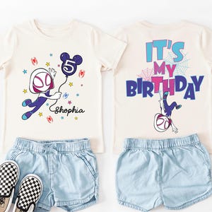 May include: A cream-colored t-shirt with a graphic of a superhero holding a number 5 balloon, paired with denim shorts and checkered sneakers. The back of the shirt says "It's My Birthday".