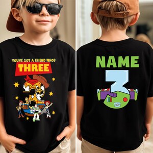 May include: Black t-shirt with a colorful graphic featuring characters and text from the movie "Toy Story." The front of the shirt says "You've Got a Friend Who's Three." The back has the word "Name" and the number "3."