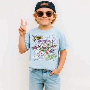 May include: A light blue t-shirt featuring Buzz Lightyear from Toy Story. The graphic shows Buzz in his spacesuit with the text "Buzz Lightyear" and "To Infinity and Beyond". The shirt is worn by a child.