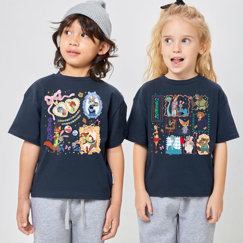 May include: Two navy blue t-shirts featuring colorful Zootopia character graphics. One shirt has "Zootopia" text, the other "Zootopia 2". The shirts have short sleeves and are worn by children.
