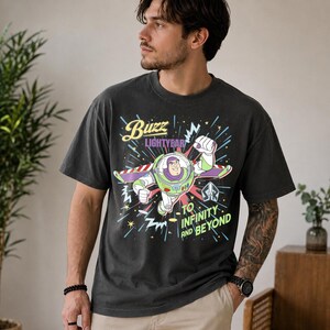 May include: Dark grey t-shirt featuring Buzz Lightyear from Toy Story. The graphic shows Buzz in flight with the text "Buzz Lightyear" and "To Infinity and Beyond". The shirt has a relaxed fit and is made of a soft material.