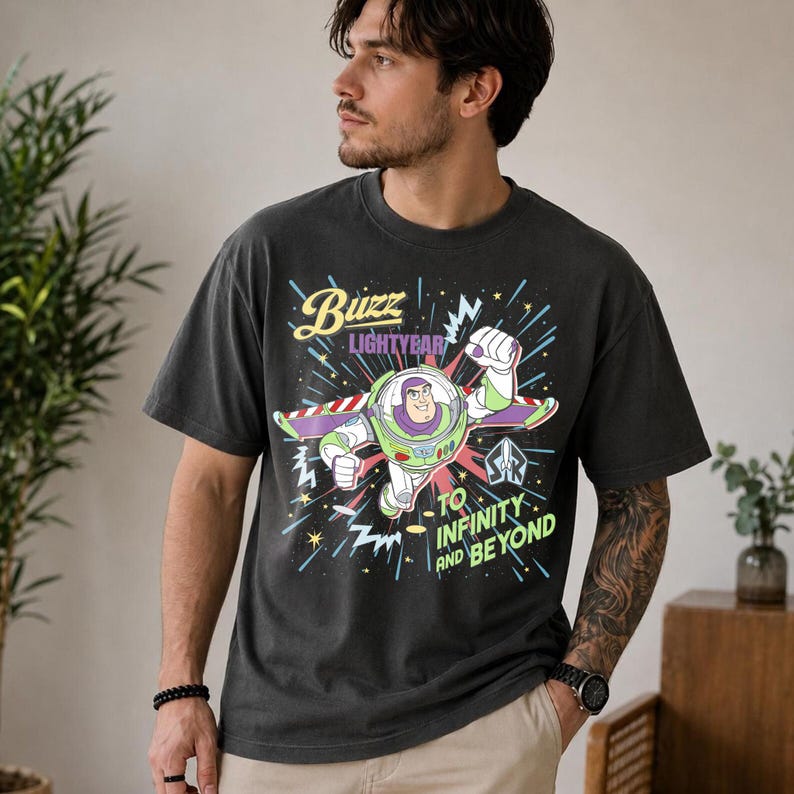 May include: Dark grey t-shirt featuring Buzz Lightyear from Toy Story. The graphic shows Buzz in flight with the text "Buzz Lightyear" and "To Infinity and Beyond". The shirt has a relaxed fit and is made of a soft material.