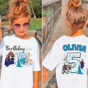Puede incluir: Una camiseta blanca con un gr&aacute;fico frontal con el texto Birthday Girl e ilustraciones de personajes de Frozen. El gr&aacute;fico trasero muestra el nombre Olivia, el n&uacute;mero 5 y otras ilustraciones de personajes con detalles de copos de nieve.