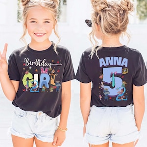 May include: Black t-shirt with the words "Birthday Girl" and a colorful graphic. The back of the shirt has the name "Anna" and the number "5". The shirt is worn by a young girl.