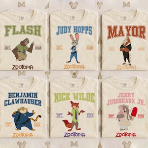 May include: Six off-white t-shirts featuring characters from the movie "Zootopia." Each shirt has a character's name in a collegiate font, the word "Zootopia," and the year "2016." Characters include Flash, Judy Hopps, Mayor, Benjamin Clawhauser, Nick Wilde, and Jerry Jumbeaux Jr.