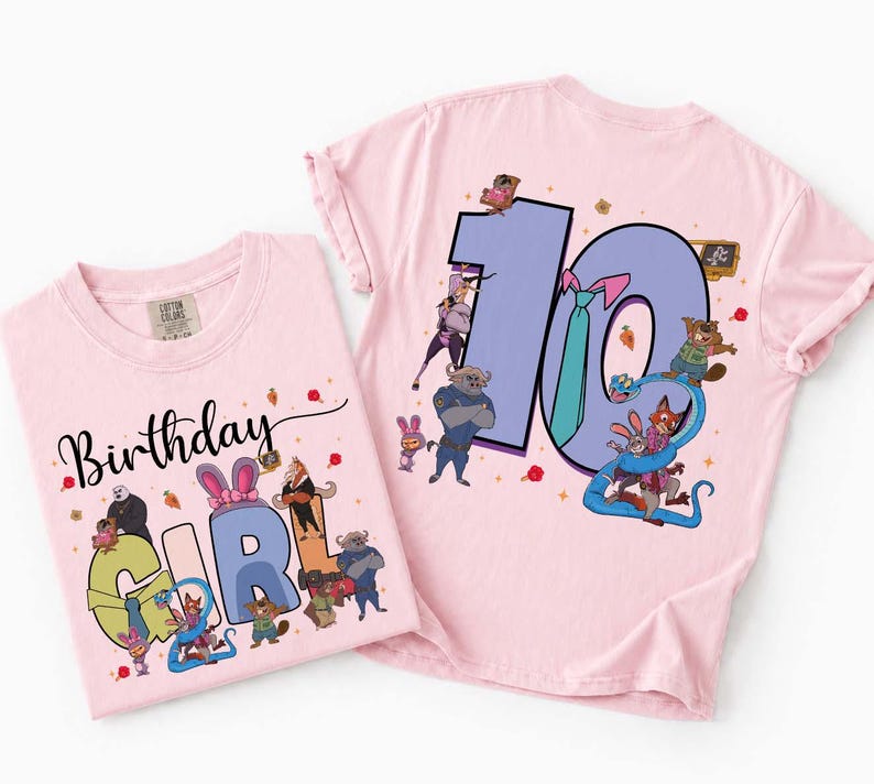 May include: Two light pink t-shirts with cartoon graphics. One shirt says "Birthday Girl" with a "2" and cartoon characters. The other shirt has a large "10" with cartoon characters. Both shirts are likely for a birthday.