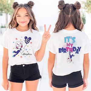 May include: White t-shirt with a colorful graphic featuring a cartoon character holding a balloon with the number 5. The front of the shirt has the name "Shopia". The back of the shirt says "It's My Birthday".