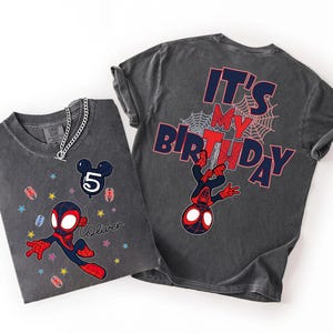 May include: Two charcoal grey t-shirts. One features a cartoon Spider-Man holding a balloon with the number 5 and the name "Oliver". The other shirt has "IT'S MY BIRTHDAY" and a Spider-Man graphic on the back. Both shirts have a distressed look.