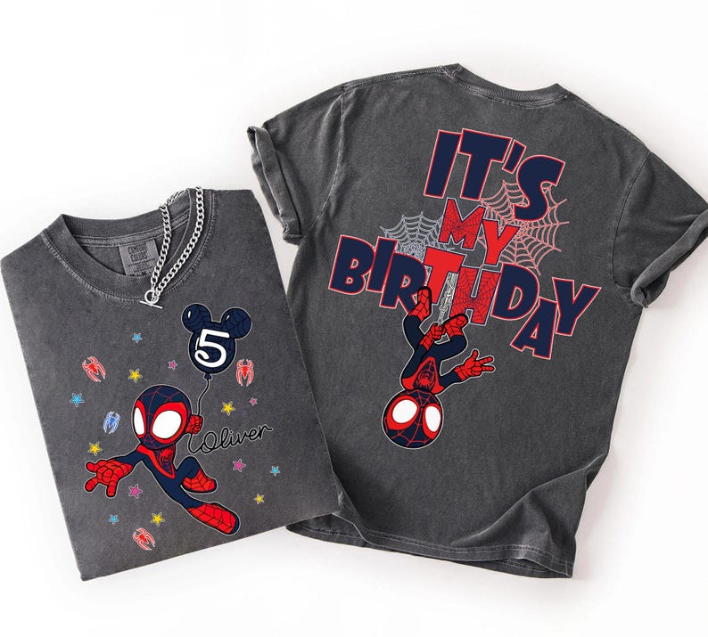 May include: Two charcoal grey t-shirts. One features a cartoon Spider-Man holding a balloon with the number 5 and the name "Oliver". The other shirt has "IT'S MY BIRTHDAY" and a Spider-Man graphic on the back. Both shirts have a distressed look.