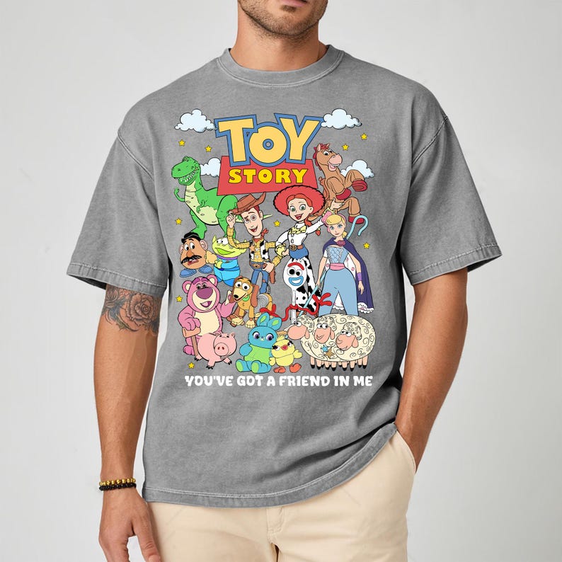 May include: Gray t-shirt featuring a colorful graphic of characters from the animated film "Toy Story." The design includes Woody, Buzz Lightyear, and other beloved characters, with the text "TOY STORY" and "YOU'VE GOT A FRIEND IN ME."