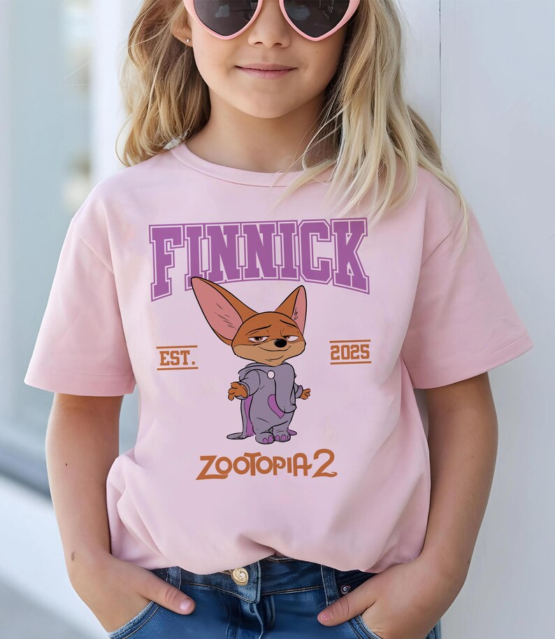 K&ouml;nnte beinhalten: Hellrosa T-Shirt mit dem Charakter Finnick aus Zootopia 2. Das Design zeigt den Namen "FINNICK" in lila Buchstaben, den Text "EST. 2025" und den Filmtitel "ZOOTOPIA 2" in Orange.