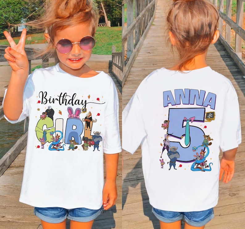 May include: A white t-shirt with the words "Birthday Girl" and a colorful graphic on the front. The back of the shirt has the name "Anna" and the number "5" in blue. The girl is wearing sunglasses and denim shorts.