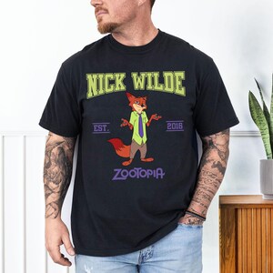 May include: Black t-shirt featuring Nick Wilde from Zootopia. The design includes the text "NICK WILDE" in green, "EST. 2016", and "ZOOTOPIA" in purple. The cartoon fox is wearing a green shirt, purple tie, and brown pants.