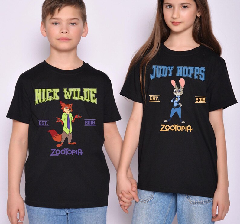 May include: Black t-shirts featuring characters from the animated film Zootopia. One shirt displays "Nick Wilde" with a fox graphic, the other says "Judy Hopps" with a bunny graphic. Both shirts have "Zootopia" and the year "2016".