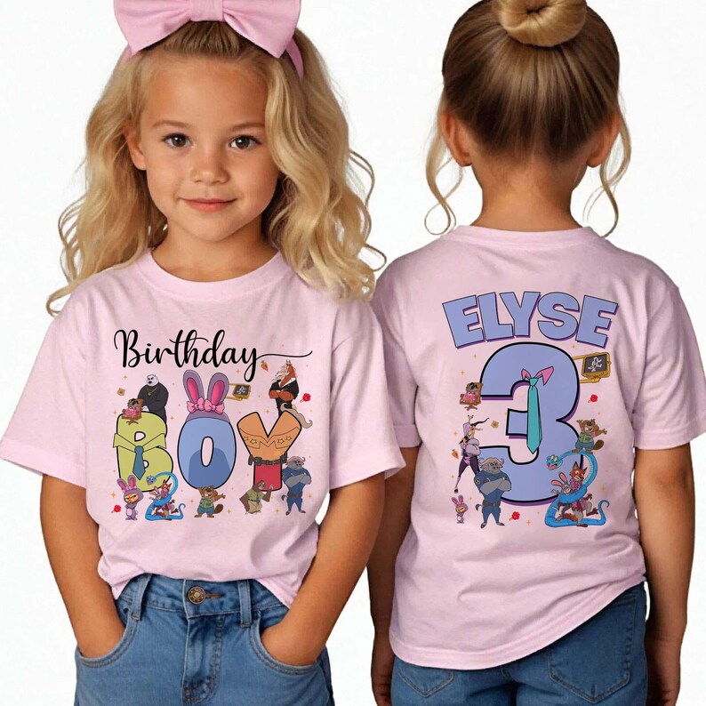 May include: Two light pink t-shirts with a birthday theme. The front shirt says "Birthday BOY" with cartoon characters. The back shirt says "ELYSE 3" with cartoon characters. The shirts are worn by a young girl.