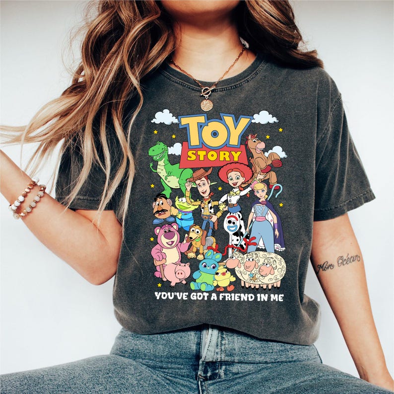May include: Dark gray t-shirt featuring a colorful graphic of characters from the animated film "Toy Story." The design includes the film's logo and the phrase "You've Got a Friend in Me."