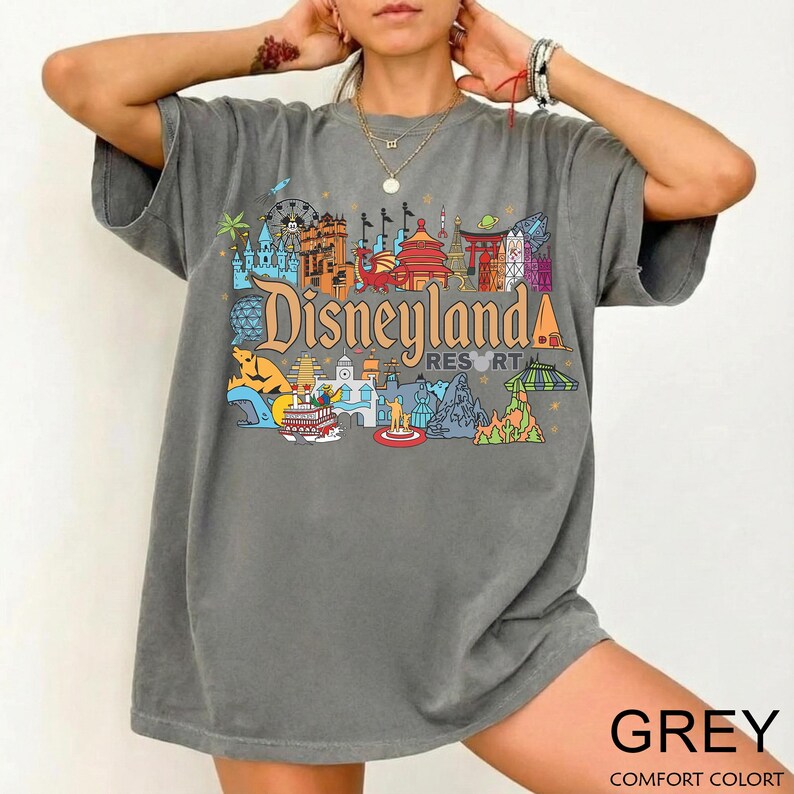 Op de afbeelding: Een grijs t-shirt met een kleurrijke Disneyland Resort-afbeelding. Het ontwerp bevat verschillende parkiconen en het Disneyland-logo. Het shirt heeft korte mouwen en een relaxte pasvorm. Het woord "GREY" staat onderaan gedrukt.