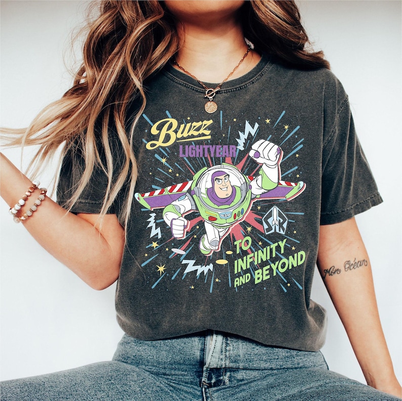 May include: Dark grey t-shirt with a graphic of Buzz Lightyear from Toy Story. The design includes the text "Buzz Lightyear" and "To Infinity and Beyond" with a colourful, retro-style illustration of the character in flight.