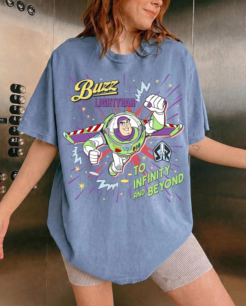 May include: A pale blue t-shirt with a graphic of Buzz Lightyear. The design includes the text "Buzz Lightyear" and "To Infinity and Beyond". The cartoon image shows Buzz in a flying pose.