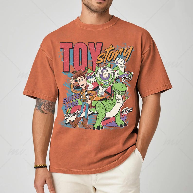 May include: Rust-colored t-shirt featuring a graphic of Toy Story characters Woody, Buzz Lightyear, and Rex. The text "TOY STORY" and "SINCE 1995" are also displayed. The shirt has a vintage, distressed look.