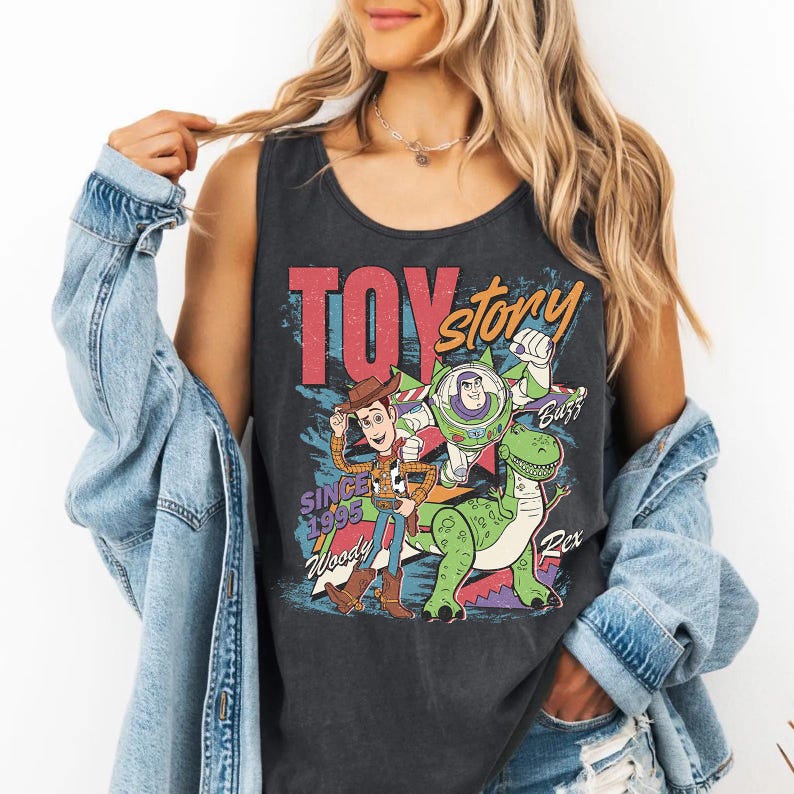 May include: Dark gray tank top featuring a graphic of characters from the movie "Toy Story." The design includes Woody, Buzz Lightyear, and Rex, with the words "Toy Story" and "Since 1995." The tank top has a vintage, distressed look.