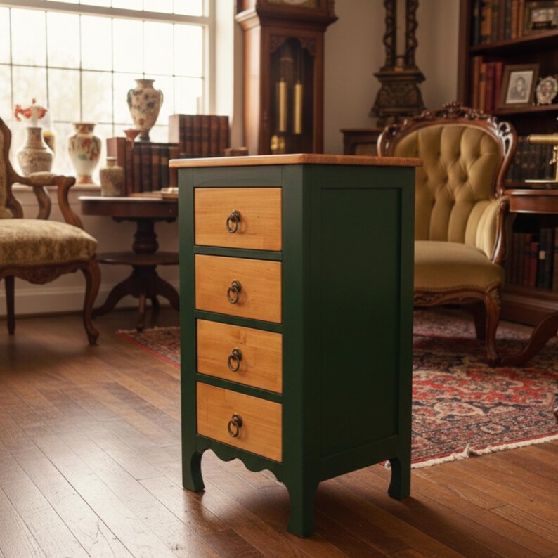 May include: A dark green wooden cabinet with four drawers. The drawer fronts are light wood, and each has a dark metal pull. The top of the cabinet is also light wood. The cabinet is in a room with a window and antique furniture.