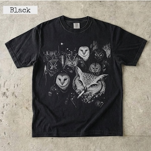 May include: A black short-sleeve t-shirt featuring a detailed graphic print of multiple owls wearing leather jackets. One prominent owl in the foreground is depicted with a cigarette in its beak. The design is rendered in shades of white and gray.