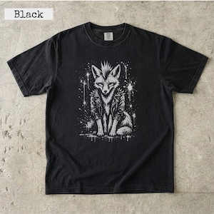 Puede incluir: Una camiseta negra de manga corta con un estampado gráfico blanco de un zorro con cresta que lleva una chaqueta de cuero con tachuelas. El diseño incluye efectos de salpicaduras de pintura blanca que rodean la ilustración del zorro.