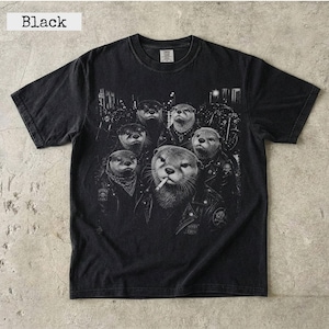 Könnte beinhalten: Ein schwarzes Kurzarm-T-Shirt mit einem Grafikdruck einer Gruppe von Ottern in Lederjacken. Der zentrale Otter hat eine Zigarette im Mund. Das Design zeigt Motorräder im Hintergrund und den Text Black.