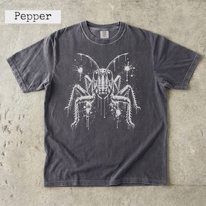Può includere: Una t-shirt a maniche corte grigio antracite con una stampa grafica bianca di una cavalletta con dettagli a schizzi d'inchiostro. La maglietta ha un girocollo e un aspetto sbiadito. La parola Pepper è stampata nell'angolo in alto a sinistra.