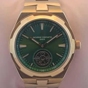 May include: A gold wristwatch with a green face. The watch has a gold strap and a round face with the brand name "VACHERON CONSTANTIN GENEVE" printed on it. The watch features a detailed design with a small, intricate pattern at the center of the face.