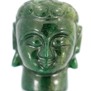 May include: A carved jade Buddha head sculpture. The sculpture is a deep green color with variations in tone. The Buddha has closed eyes, a serene expression, and detailed facial features. The head is mounted on a short, cylindrical base.
