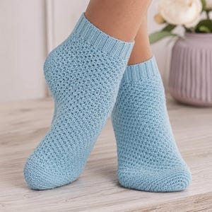 May include: A pair of light blue ankle socks featuring a textured, crocheted-style knit pattern with a ribbed cuff at the top. The socks are crafted from a solid-colored yarn and provide a snug fit around the foot, showcasing a consistent stitch.