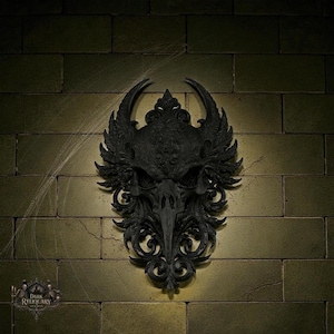 May include: A black gothic wall sculpture featuring a bird skull design with ornate details. The sculpture has wing-like elements and decorative flourishes. The piece is mounted on a brick wall, and the logo "Dark Reliquary" is visible in the lower left corner.