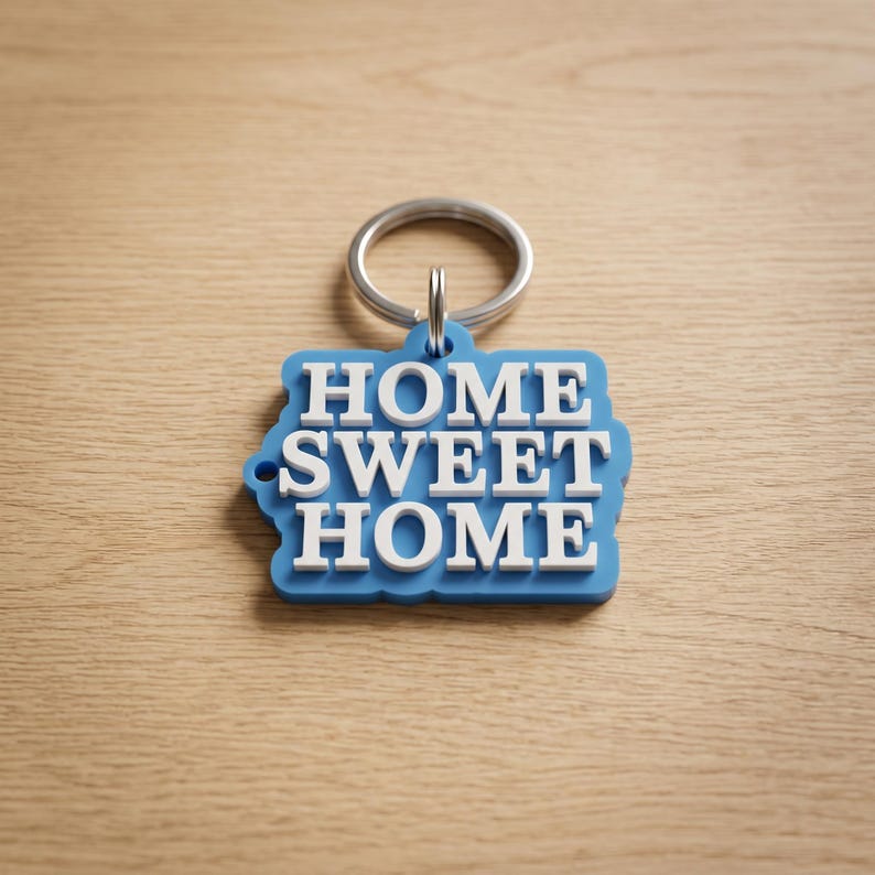 May include: A blue keychain with the words "HOME SWEET HOME" in white lettering. The keychain has a silver ring attached to it. The background is a light brown wooden surface.