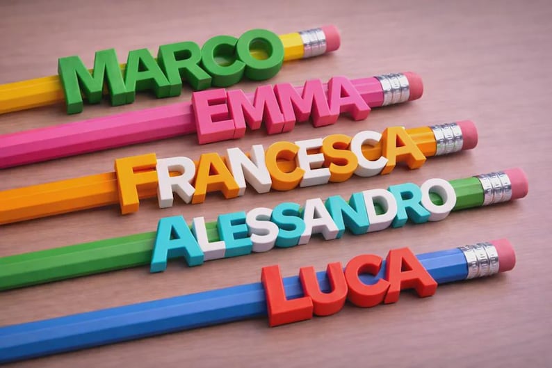 May include: Colorful pencils with names: Marco, Emma, Francesca, Alessandro, and Luca. Each pencil is a different color, with the name spelled out in 3D letters. The pencils have erasers and silver metal bands.