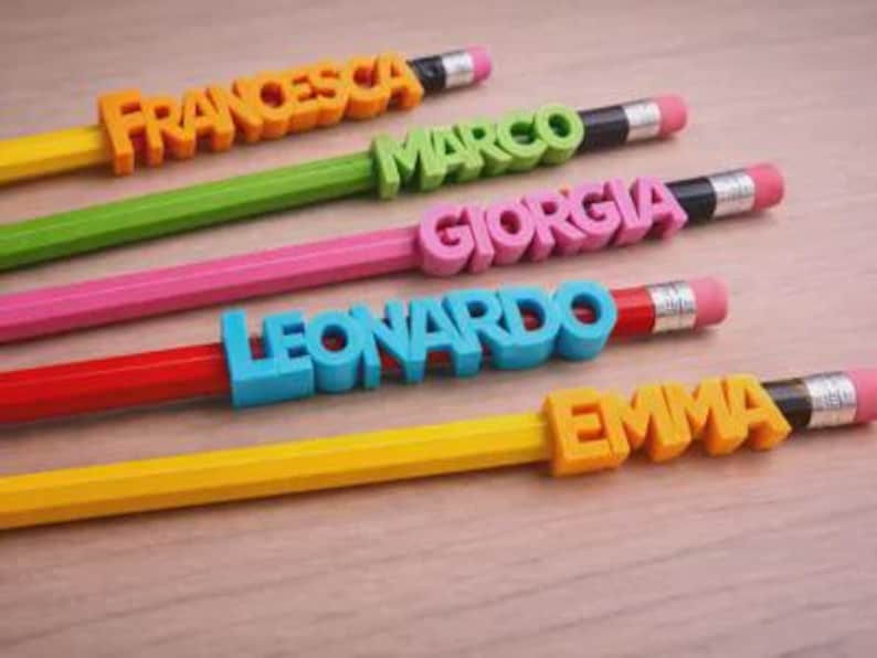 May include: Five colorful pencils with names: "FRANCESCA", "MARCO", "GIORGIA", "LEONARDO", and "EMMA" in orange, green, pink, blue, and yellow. Each pencil has a different color and a pink eraser.
