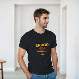 Peut inclure: T-shirt noir à col rond avec le texte "ERROR 404" en jaune et rouge, avec la légende "//motivation not found" et un symbole d'avertissement. Le t-shirt est porté par une personne.
