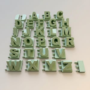 May include: A full alphabet set of light green interlocking letter blocks. Each letter is in a bold, sans-serif font and has a unique interlocking design. The letters are arranged in rows and columns on a light background.