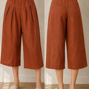 May include: Rust-colored wide-leg culottes featuring an elasticized waistband, front pleats, and a V-shaped back yoke seam. These cropped trousers have a loose, flowing silhouette that falls below the knee, providing a comfortable fit.