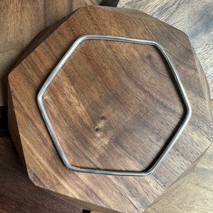 May include: A silver hexagon-shaped bangle bracelet on a wooden surface.