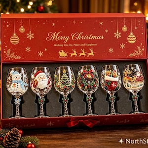 May include: A set of six clear wine glasses in a red gift box. Each glass features a unique Christmas-themed design including a snowman, Santa Claus, a tree, a wreath, a stocking, and a reindeer. The box lid reads Merry Christmas.