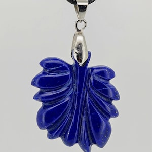 May include: A deep blue leaf-shaped pendant necklace. The pendant is carved with detailed veining and hangs from a black cord. The pendant is attached to a silver-colored metal bail.